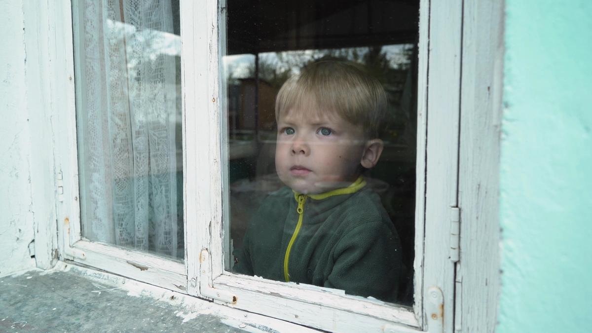 A sad boy looking out of a window