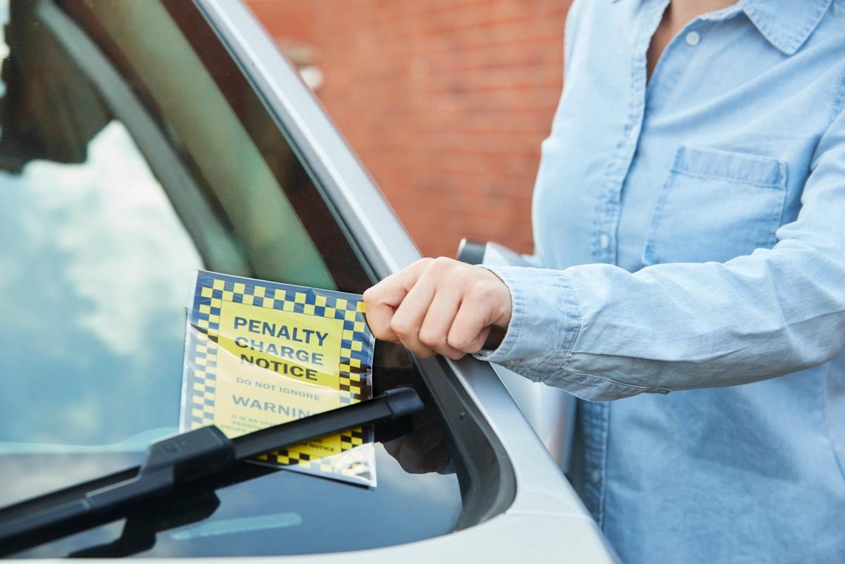 A woman pulls a parking fine from under her windscreen wiper