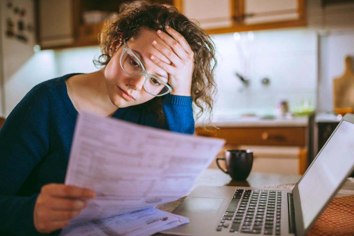 A worried-looking woman goes through her bills in the kitchen