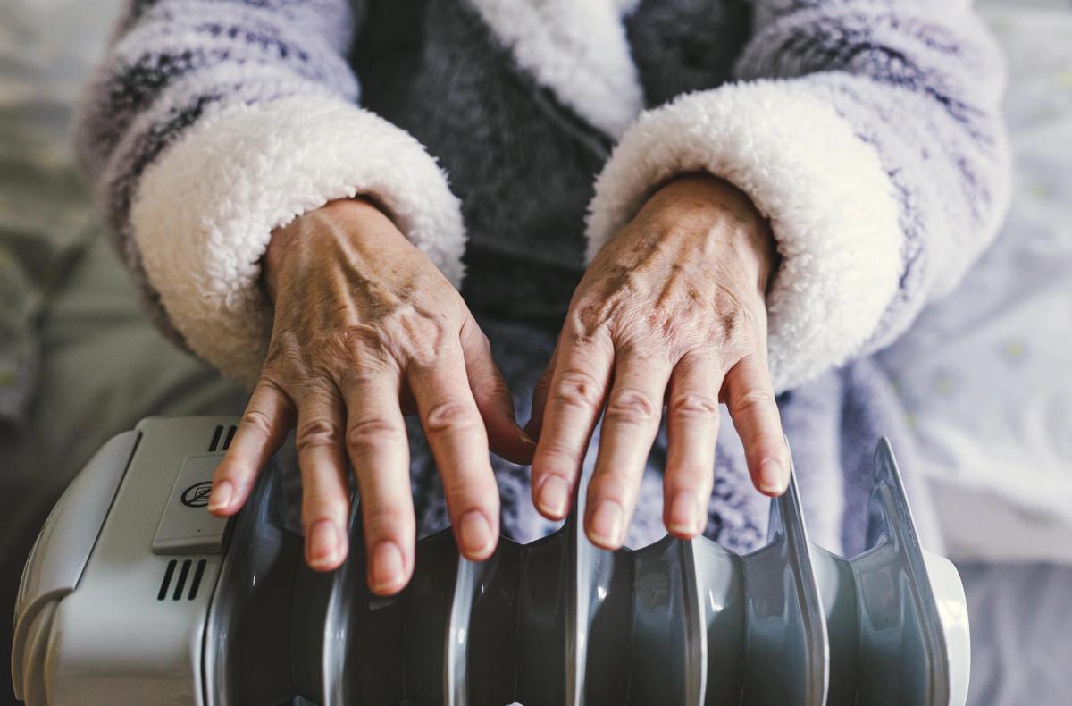 Old woman warming her hands over an electric heater