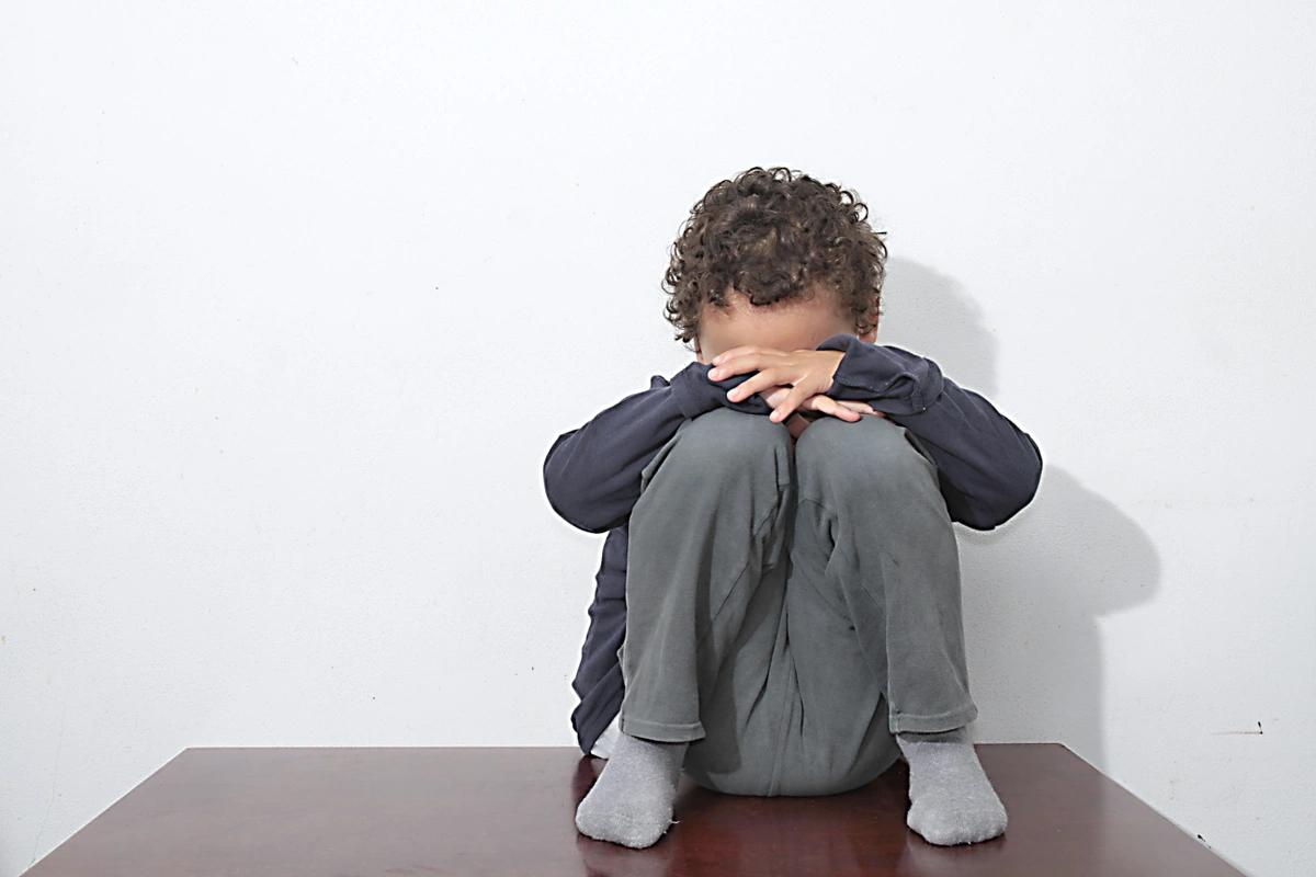 A young boy sits on the floor with his head in his hands