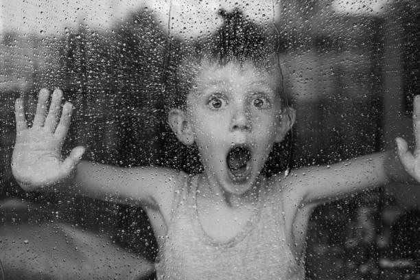 Image of a little boy stood at a window with the rain pouring down