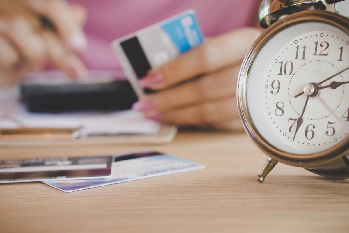 Person using calculator holding credit card next to alarm clock