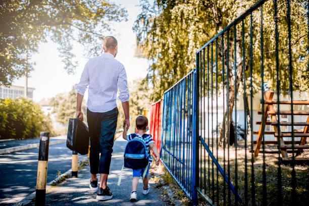 image of a man walking down the street carrying a brief case and holding a child's had who has his school bag