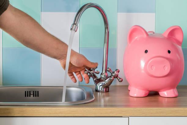 Image of someone running a tap next to a pink piggy bank