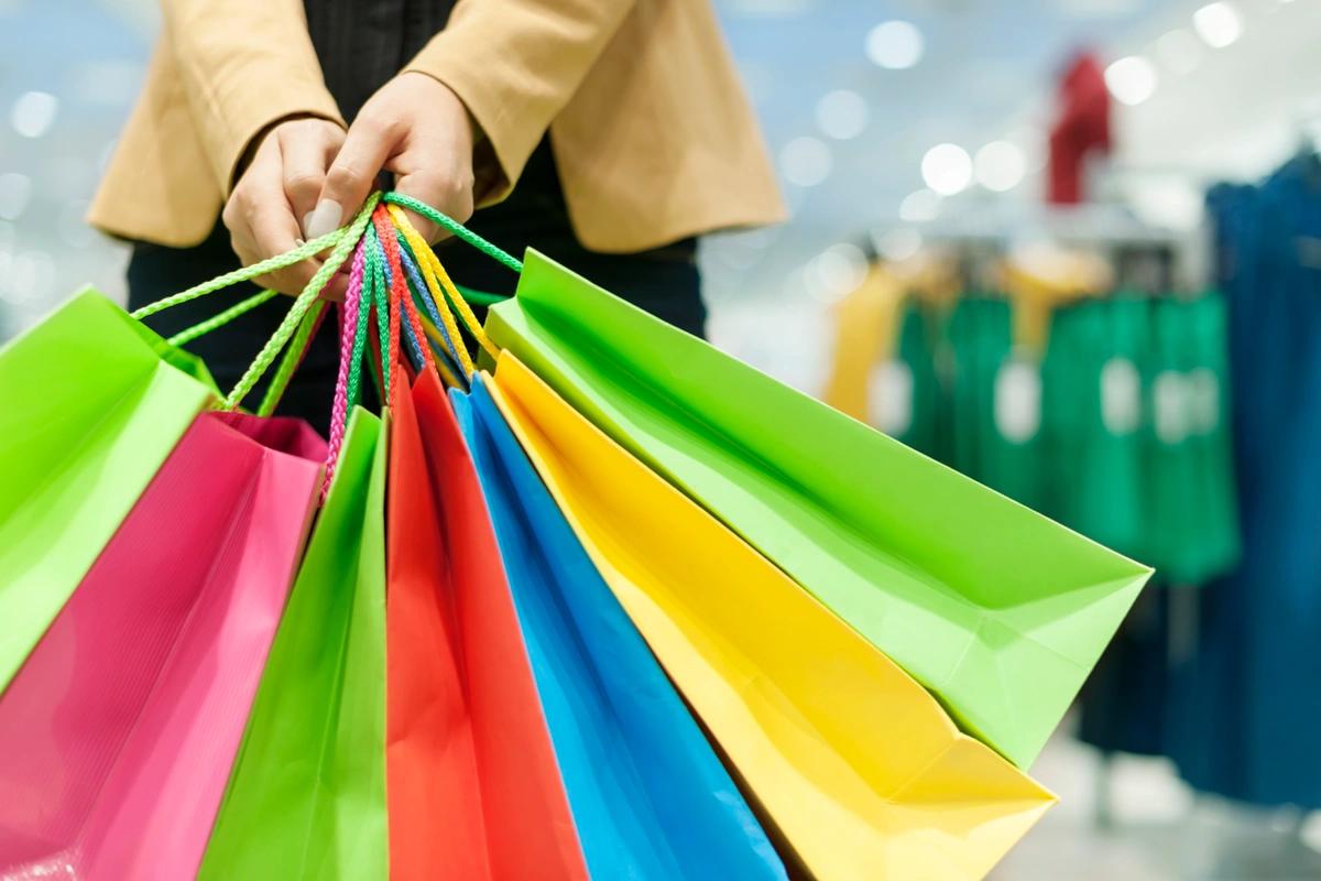 A close up of a woman clutching lots of brightly coloured paper shopping bags.