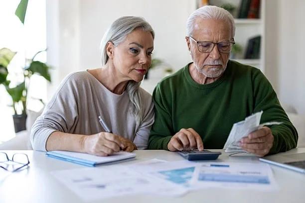 Image of two pensioners assessing pension paperwork. Pension savers could be owed thousands after paying too much tax - how to check. More than £44 million has been refunded to people who accessed pension savings, after tax was overpaid on their with
