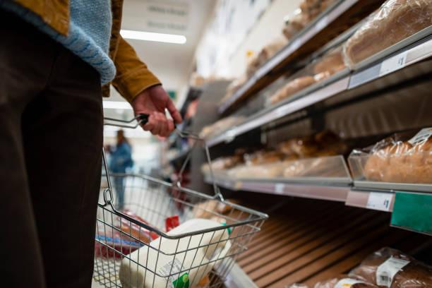 Image of a man carrying a supermarket basket containing milk in front of the bread aisle