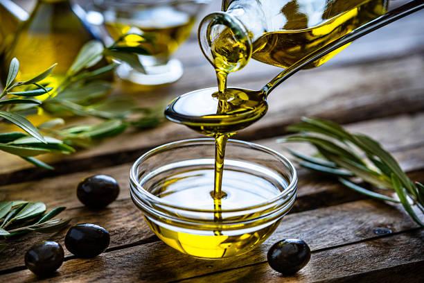 Image of olive oil being poured from a bottle into a bowl with olives and branches around. Olive oil soars in price. What are the cheaper alternatives and how can olive oil be used other than cooking
