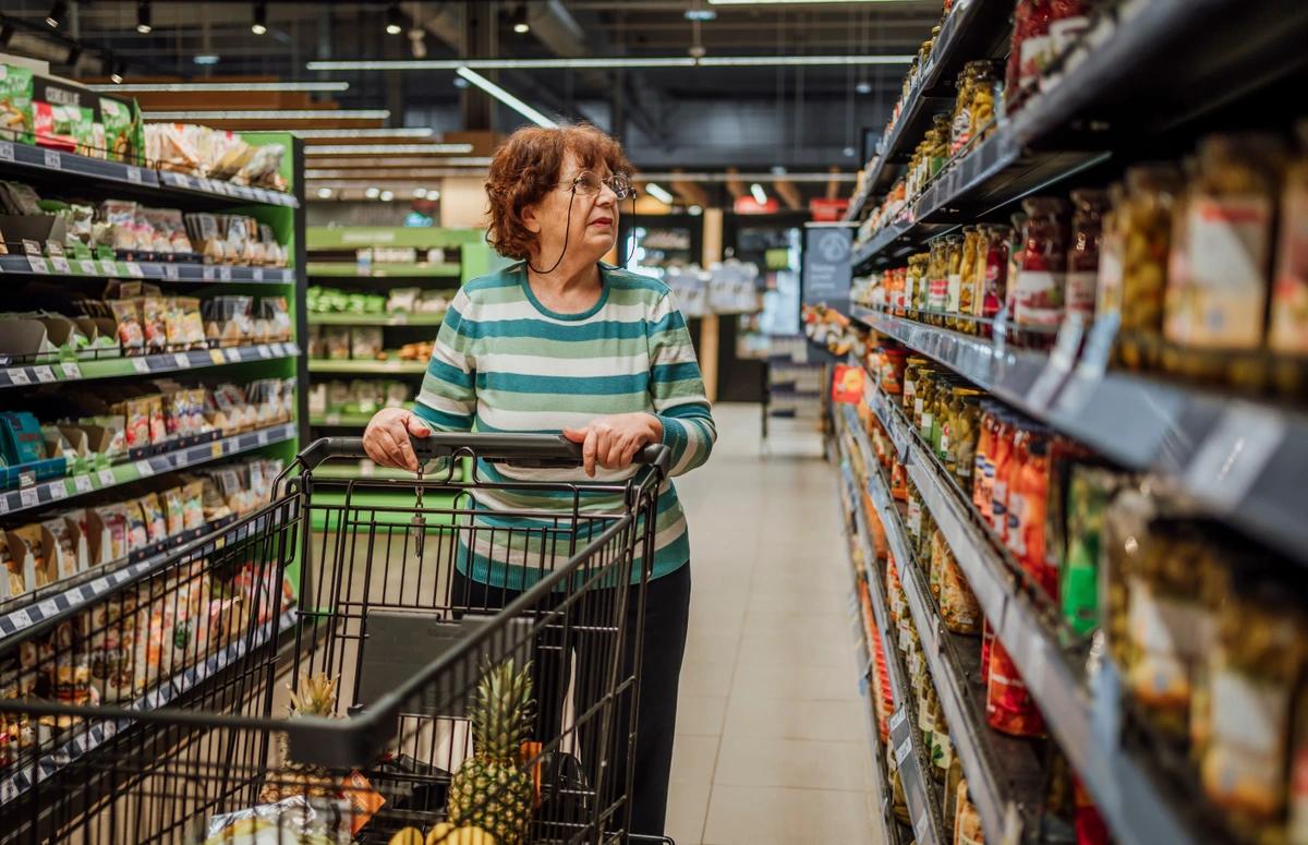 Woman pushing trolley between supermarket shelves