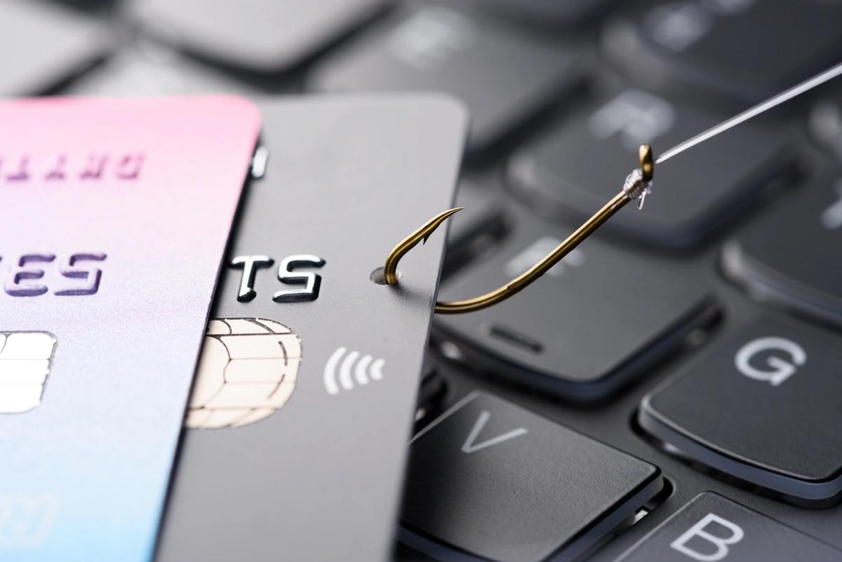 A fishing hook dragging stolen credit cards across a computer keyboard