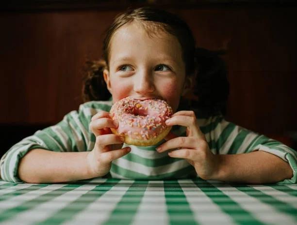 Image of a child eating a donut. Parents face a £44 ‘snack attack’ during school holidays. Find out where you can get help with creeping school holiday costs