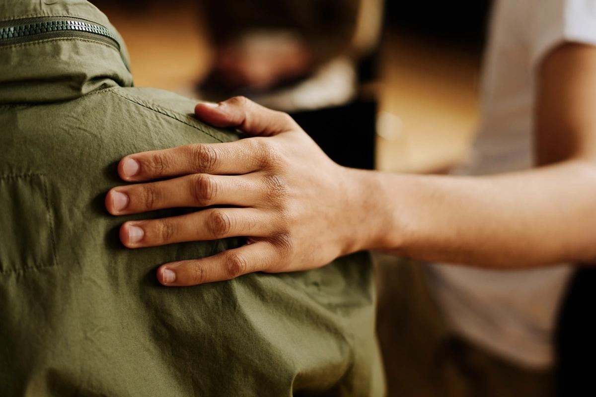 Someone places a comforting hand on a man's back