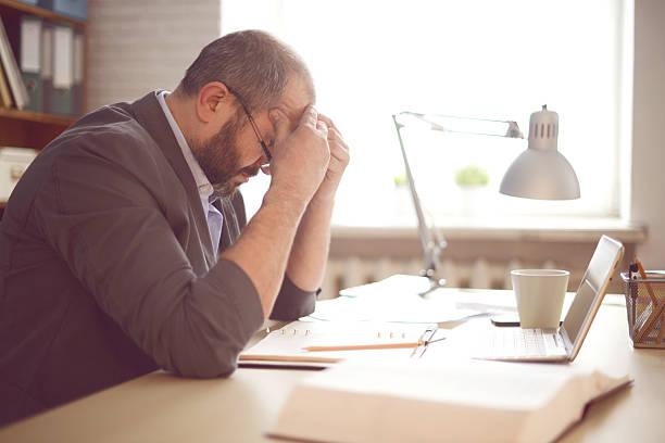Image of a man with his head in his hands looking worried at a laptop. Working and in debt. What financial support is available for people working. Debt advice for working people