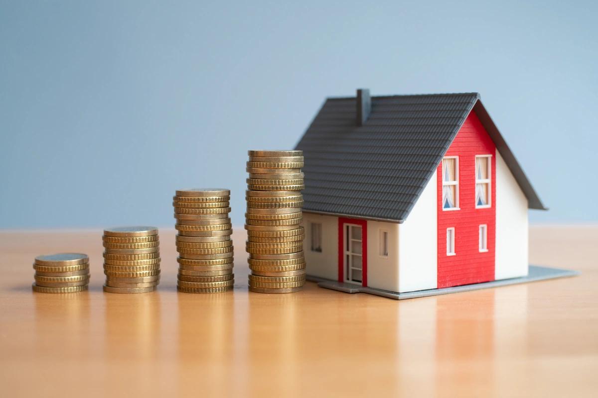Ascending stacks of coins next to a model house on a table