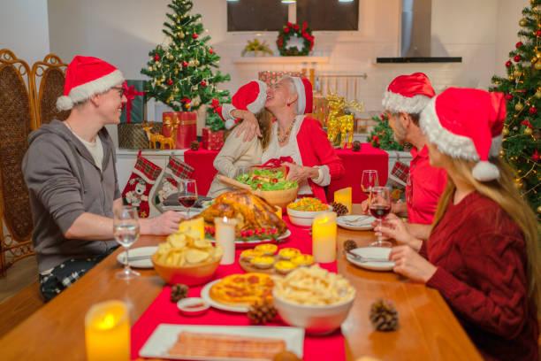 Image of a family sat around a dinner table with Christmas hats on and a huge Christmas lunch in front of them