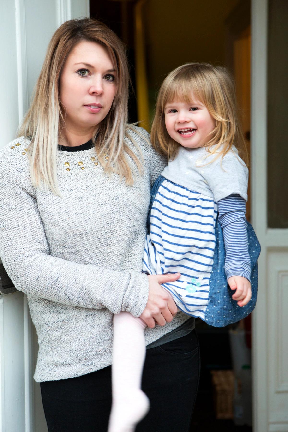 A mother and her young daughter stand in the doorway of their home