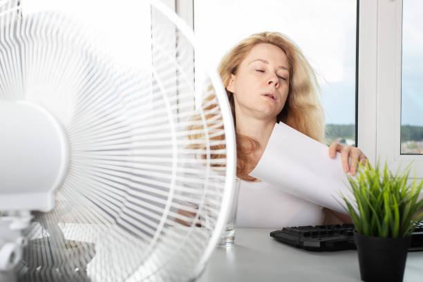 Image of someone sat in front of a fan at work. How to stay cool without burning through your budget. 10 ideas to stop you blowing your budget on the hottest day of the year