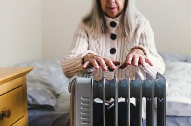 Image of a woman sat over an electric heater warming her hands