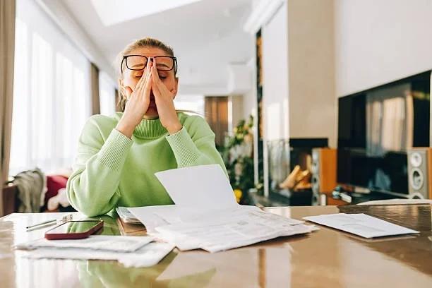 Image of a lady looking stressed surrounded by bills. Is the cost of living starting to catch up with middle earners? How figures show rising everyday costs are putting more pressure on households that once felt financially comfortable