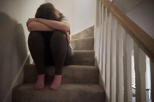 Image of a woman cowering on the stairs with her face covered. New housing rules are good news for abuse survivors, and the insolvency register should be next. The government says survivors shouldn’t have to prove their abuse again to stay safe in th
