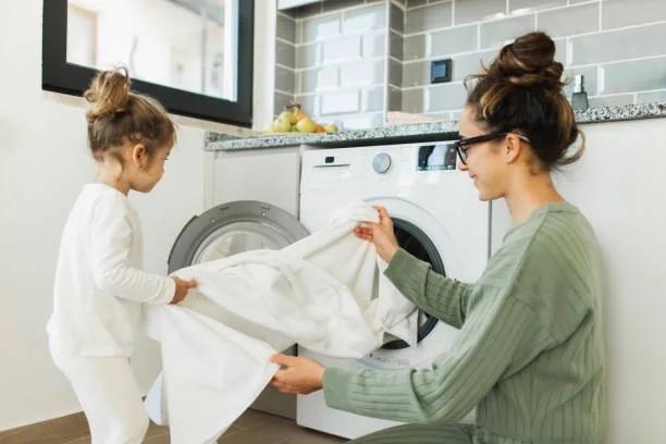 Image of a child helping her mum take out bedding from the tumble dryer. 6 easy ways to make your appliances last longer and save you £s. Help if you can't afford to replace your cooker, fridge or washer. Low income