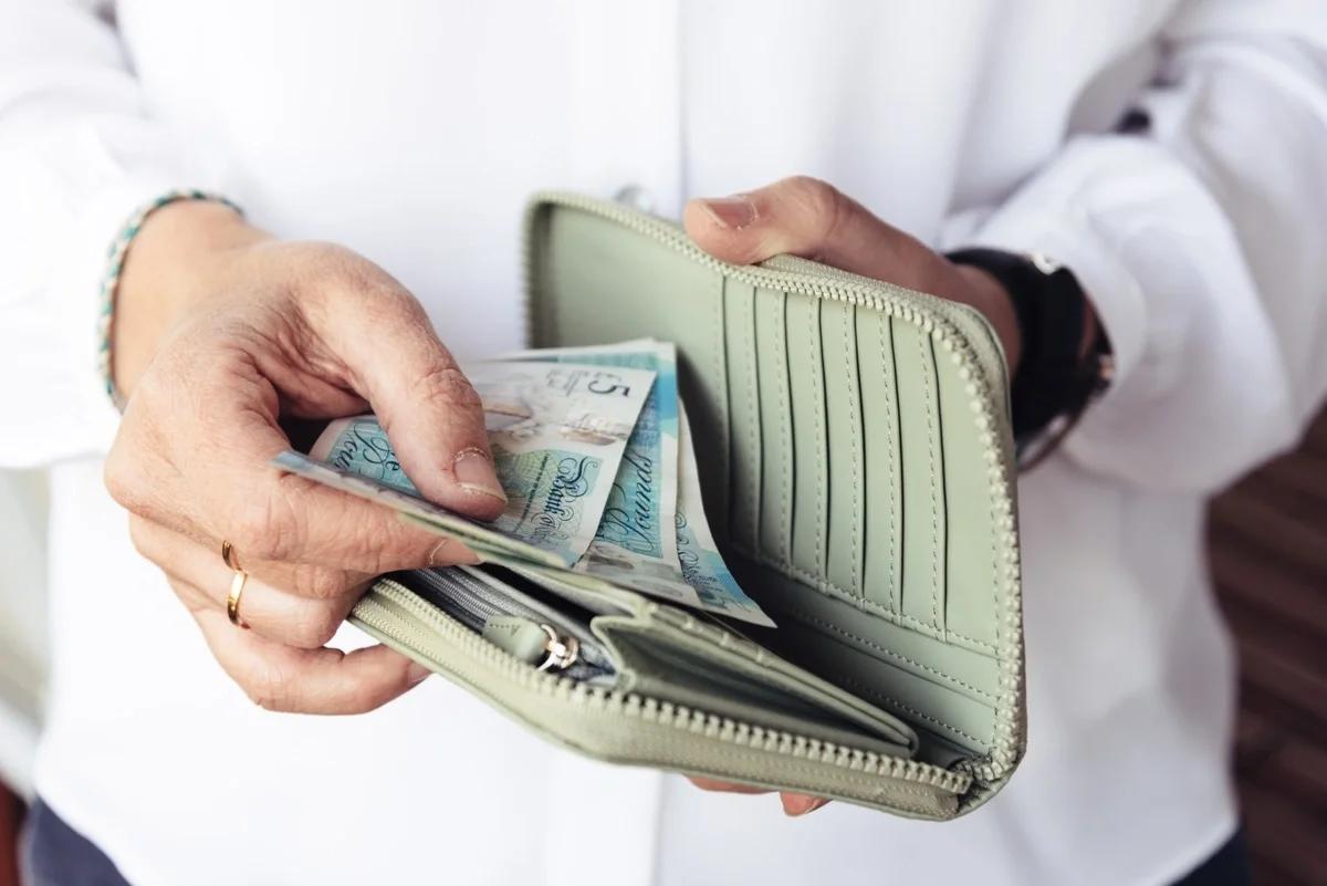 A close-up of a woman's hands putting some five pound notes into her wallet