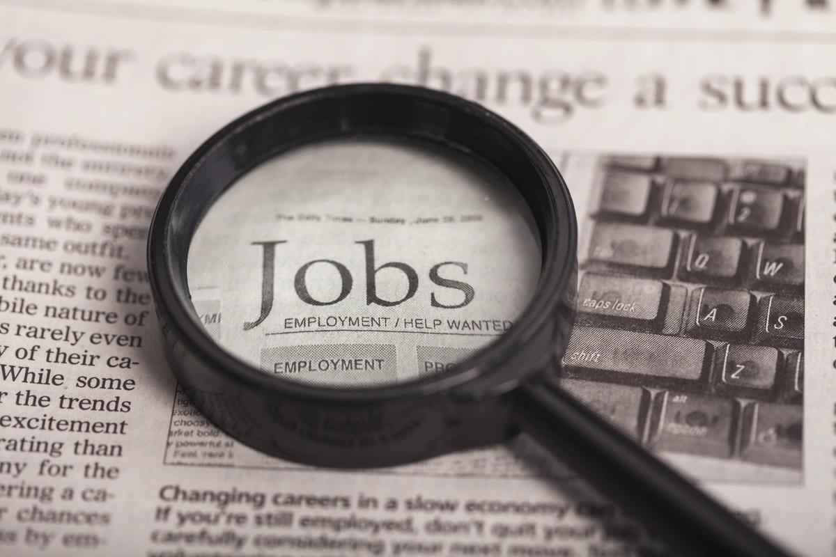 A magnifying glass placed over the word 'Jobs' in a newspaper