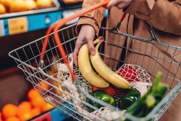 Image of someone holding a shopping basket and filling it with fruit. Aldi launches free £50 voucher scheme to help with summer holiday costs