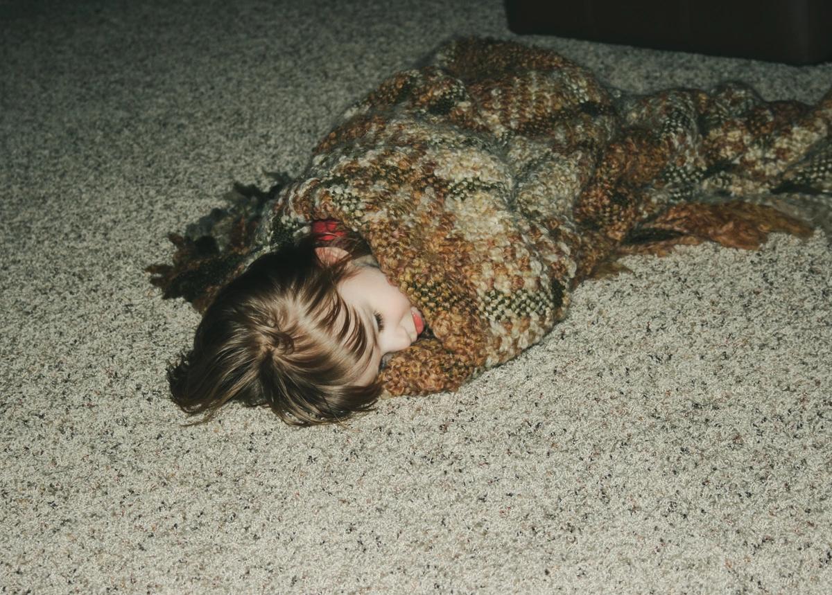 A little girl wrapped up in a blanket sleeps on the floor