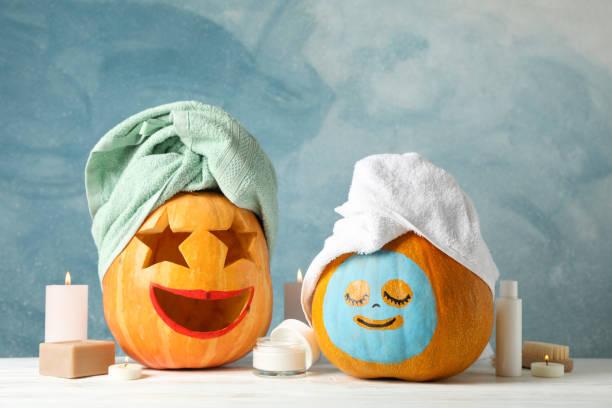 Image of two pumpkins with facemasks and hair towels on surrounded by candles