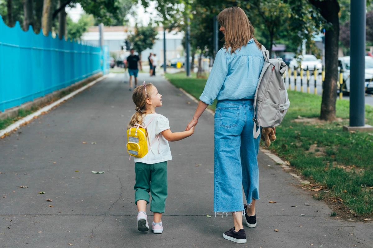 A woman and her daughter holding hands and chatting on the way to school