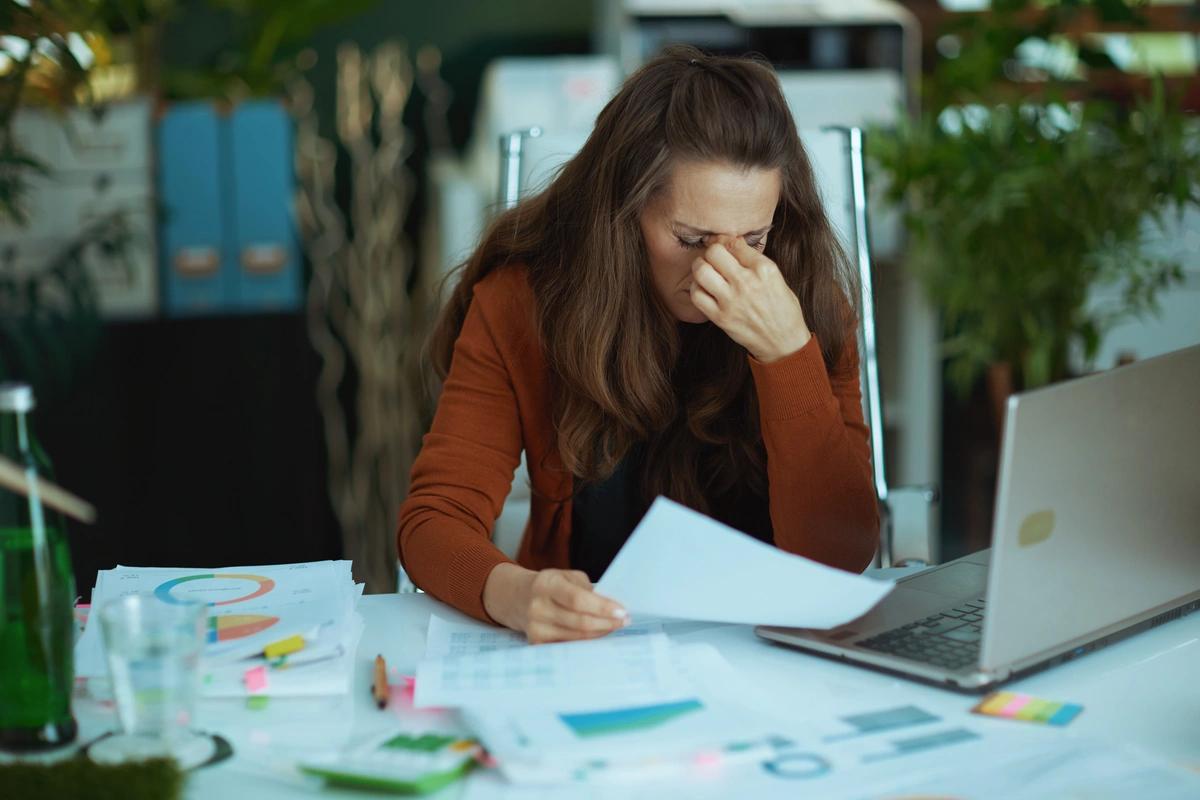 A worried-looking woman sits at a laptop going through her bills