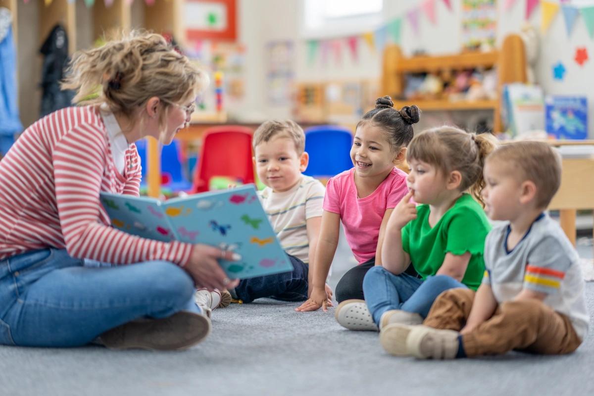 A nursery school teacher reads a book to some children