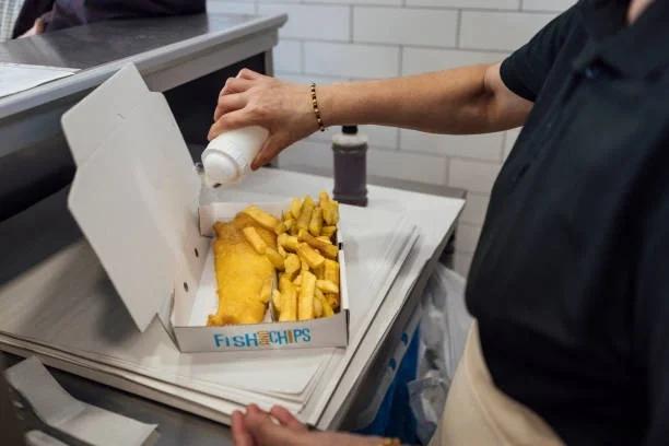 Image of fish and chips in a tray with someone covering it in salt and vinegar. The great British chippy tea is getting pricier. Here's how to save  Fish and chips now costs over £11 a portion. Here’s how to still enjoy it without breaking the bank.