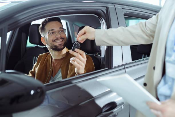 Image of a man sat in a car with the window down being given a set of keys from a man holding a contract