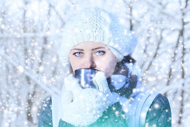 Image of a woman wrapped up warm drinking a hot drink with snow coming down around her