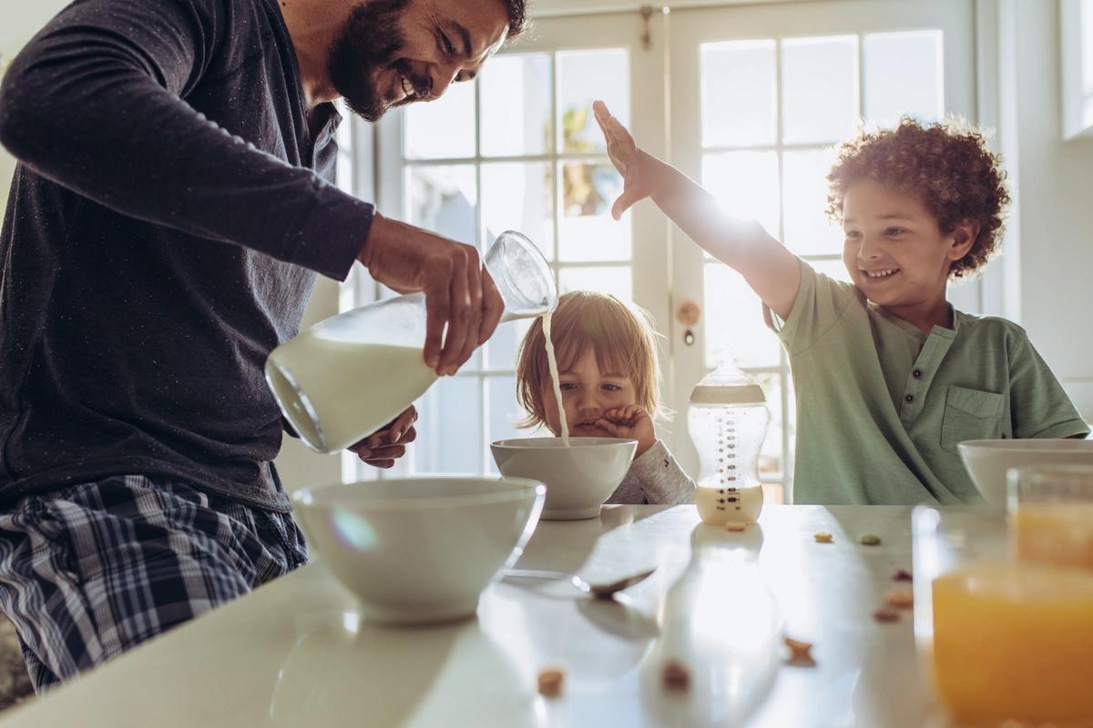 Smiling father pouring milk in to bowls for kids breakfast