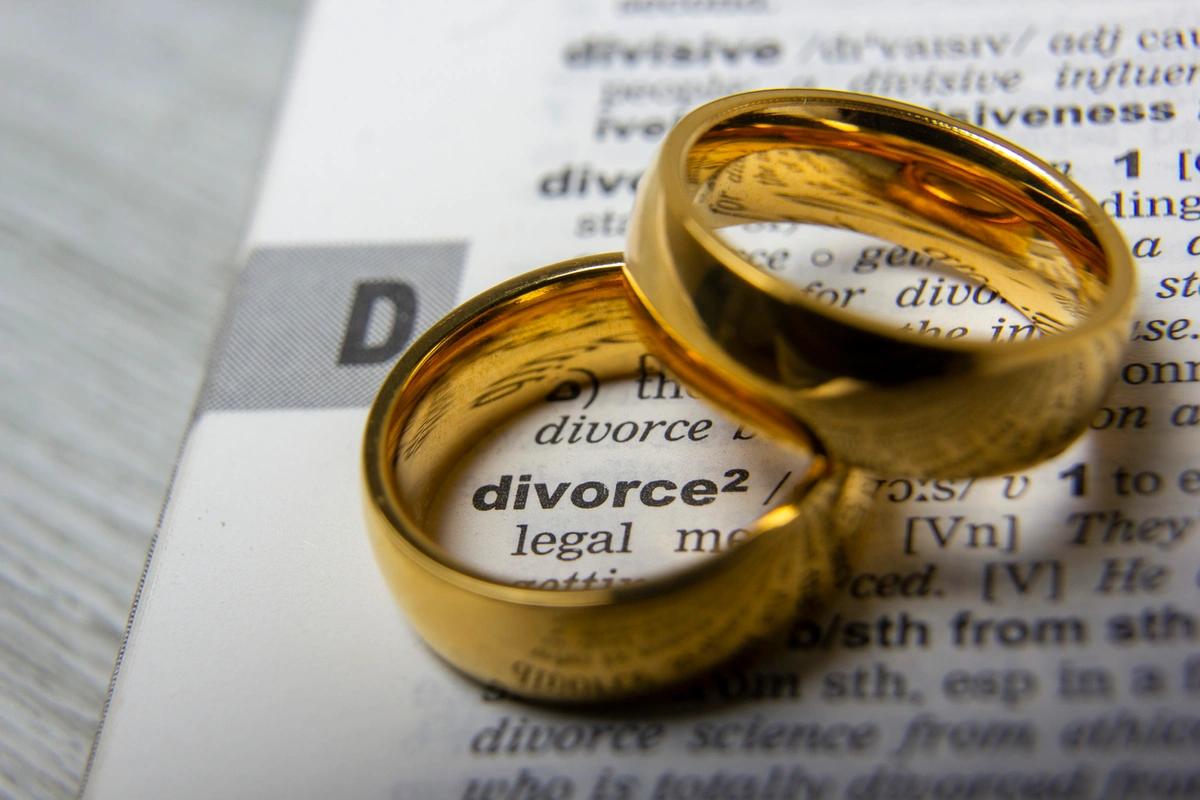 Two gold wedding rings sitting on the definition of divorce in an open dictionary