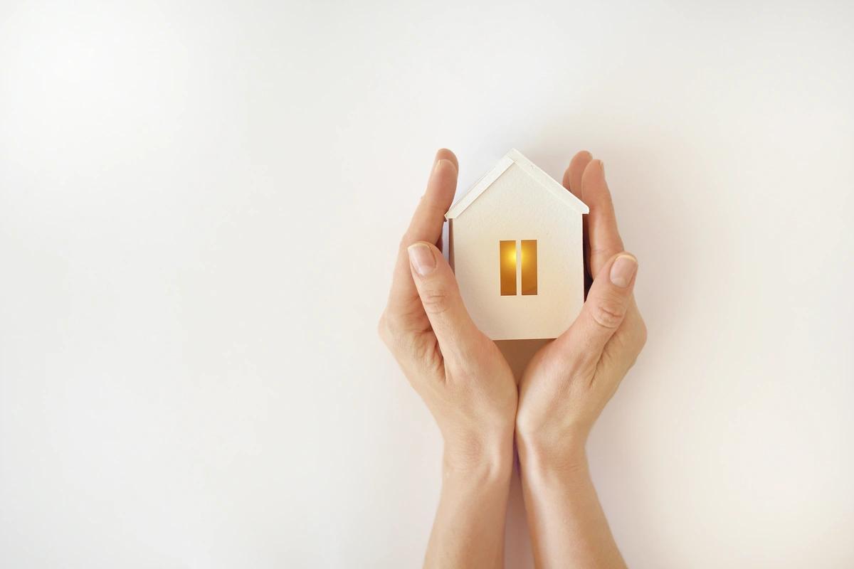 A woman's hands holding a model of a house with a warm light inside