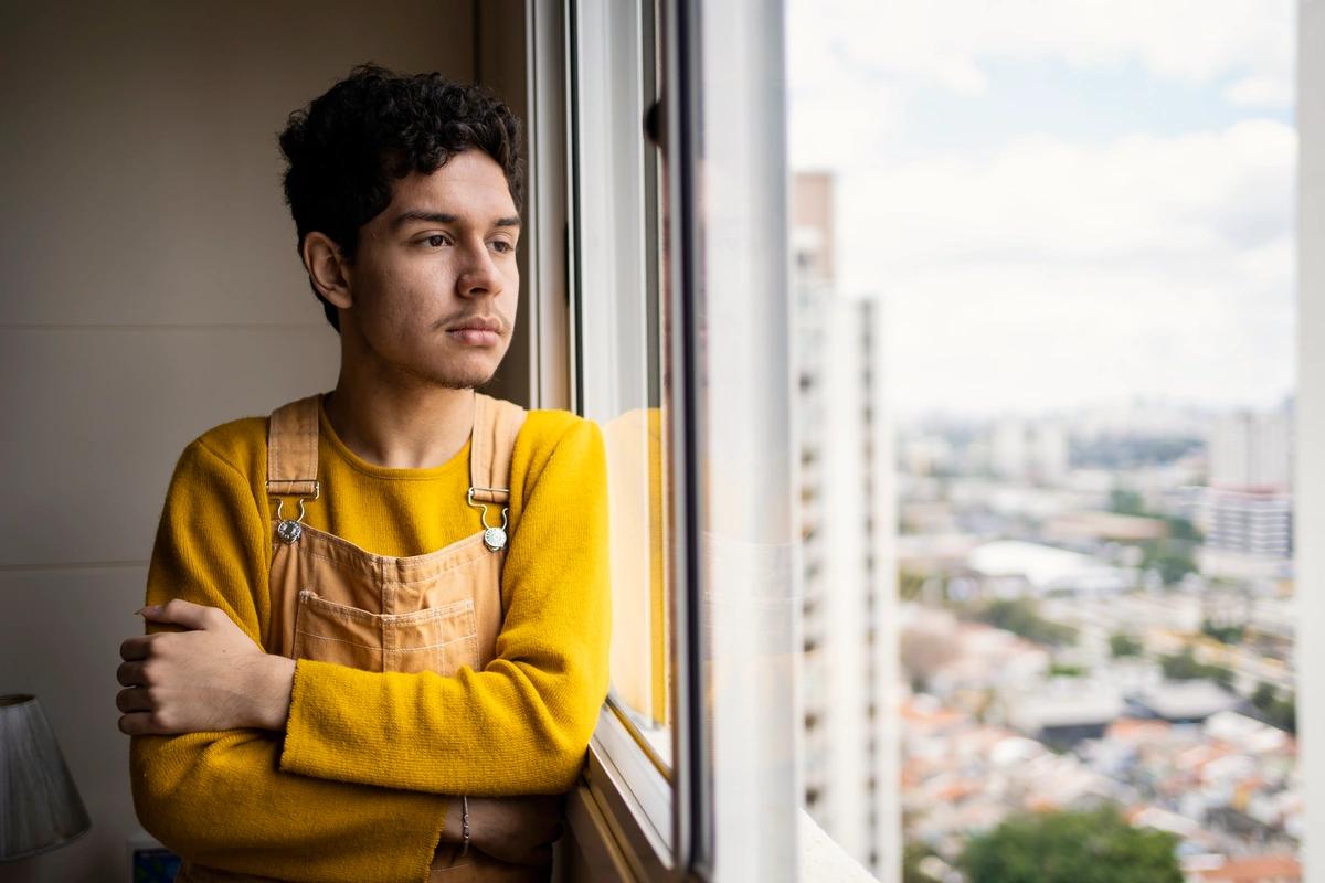 An unemployed young man living in a deprived area gazes out of the window of his flat
