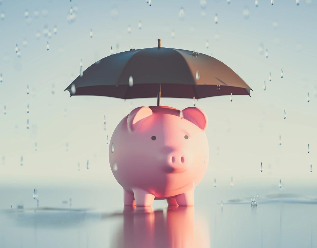 A piggy bank sheltering from the rain under an umbrella