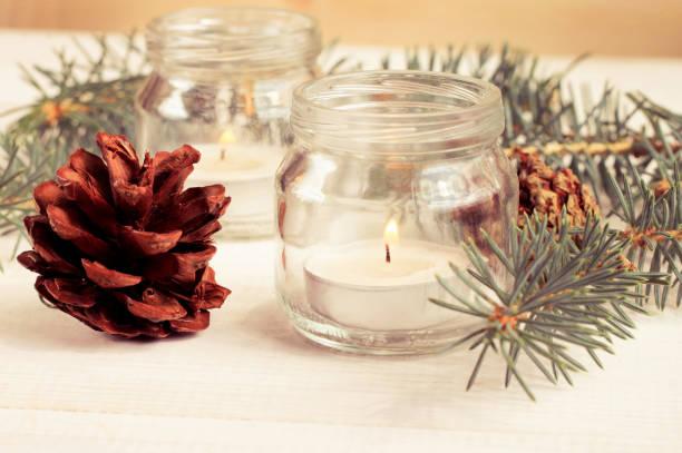 Image of tea light candles in jam jars surrounded by pine cones and fur tree branches