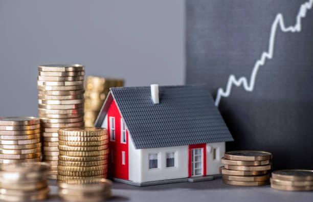 Image of piles of coins next to a toy house and a graph in the background with a line going upwards. Find out what help is available if you're struggling to pay your mortgage
