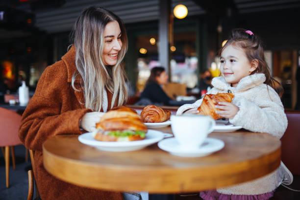 Image of a mum sat with her daughter in a cafe with sandwiches and drinks in front of them