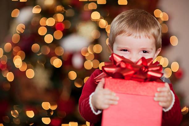 Image of a child looking happy holding out a wrapped Christmas present