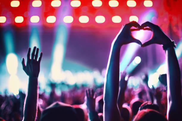 Image of a crowd at a concert with a woman holding her hands up making a heart sign with her fingers