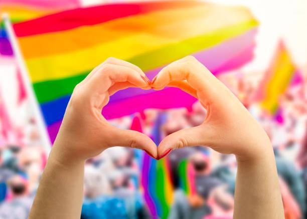 image of two hands forming a heart in front of the rainbow Pride flag