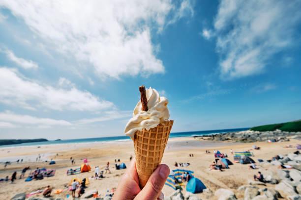 Image of a British beach with holidaymakers on it in the background and someone holding an ice cream cone in the foreground