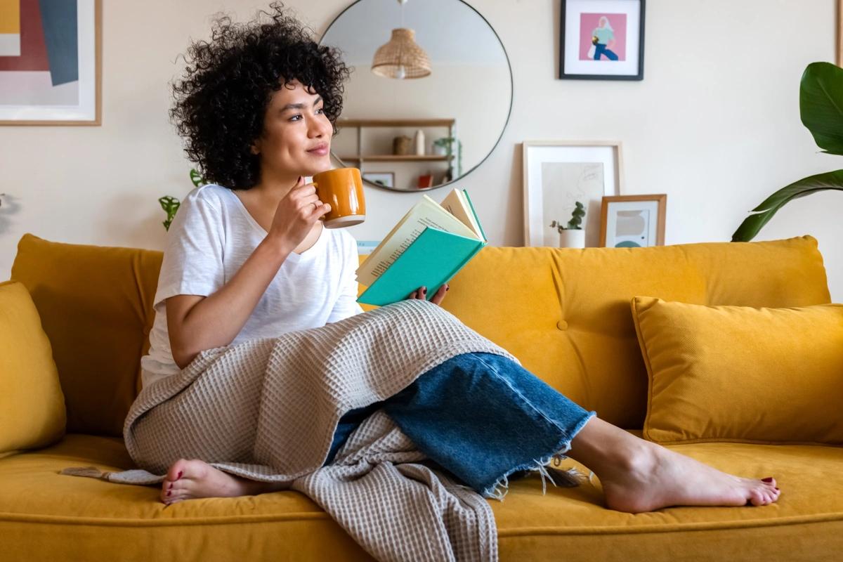 Woman curled up on a sofa with a cup of tea and a book